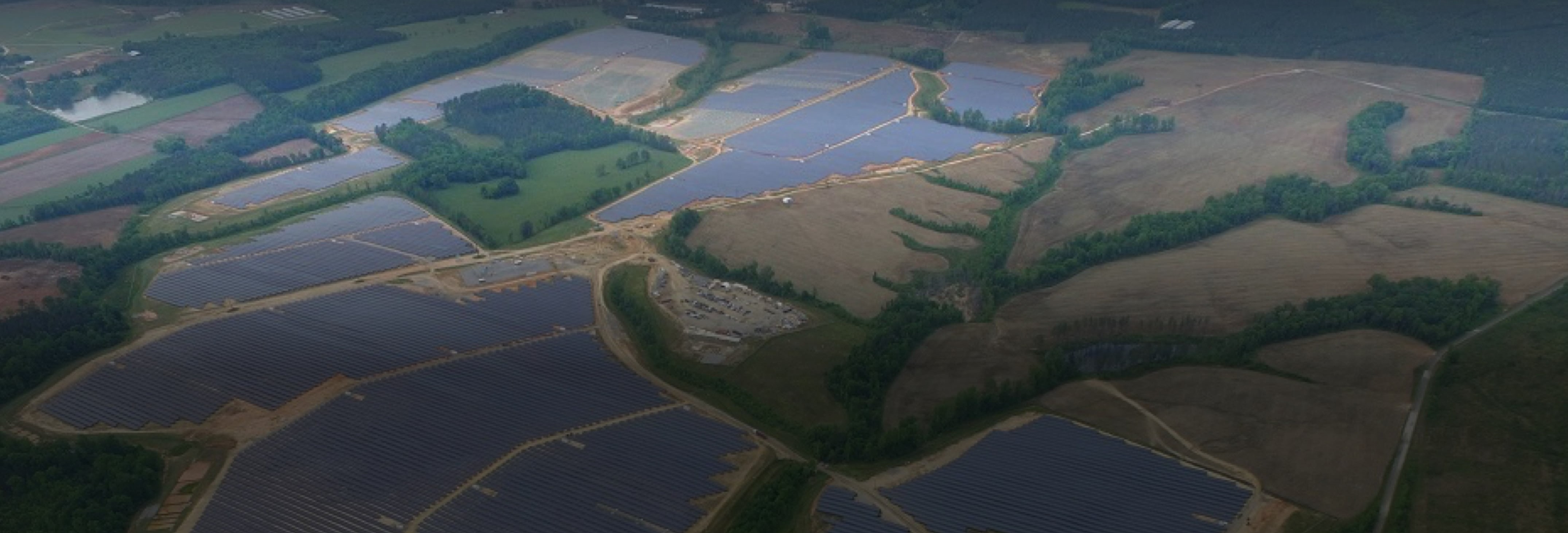 Birdseye view of large solar farm with rows of solar panels among green fields