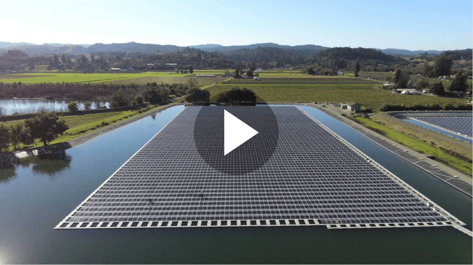 Thumbnail of a birdseye view of a solar farm floating on water with mountains in background.