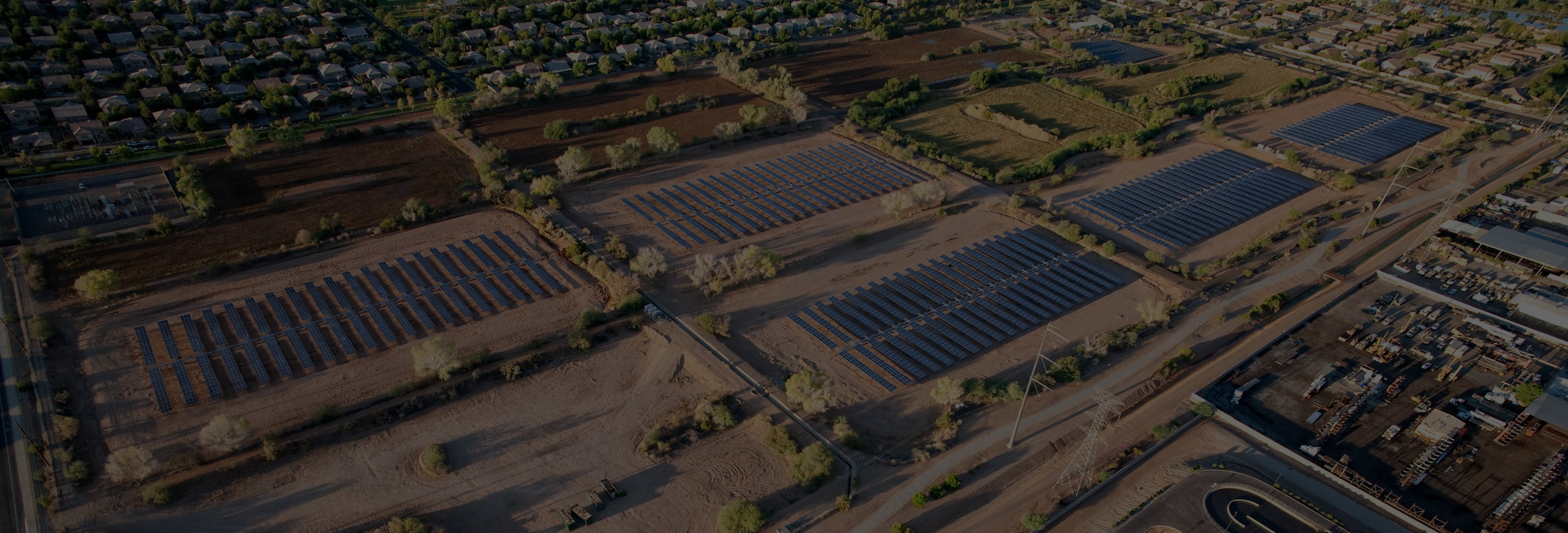Birdseye view of several solar fields with rows of blue panels surrounded by farmland and equipment.