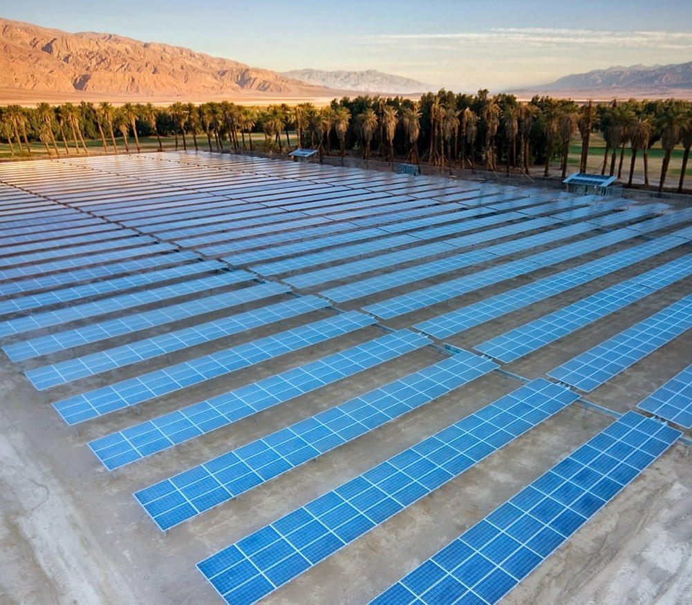 Aerial view of multiple rows of solar panels surround by trees.