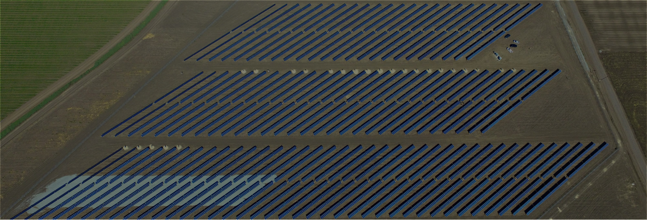 Aerial view of three rows of solar panels on farmland.