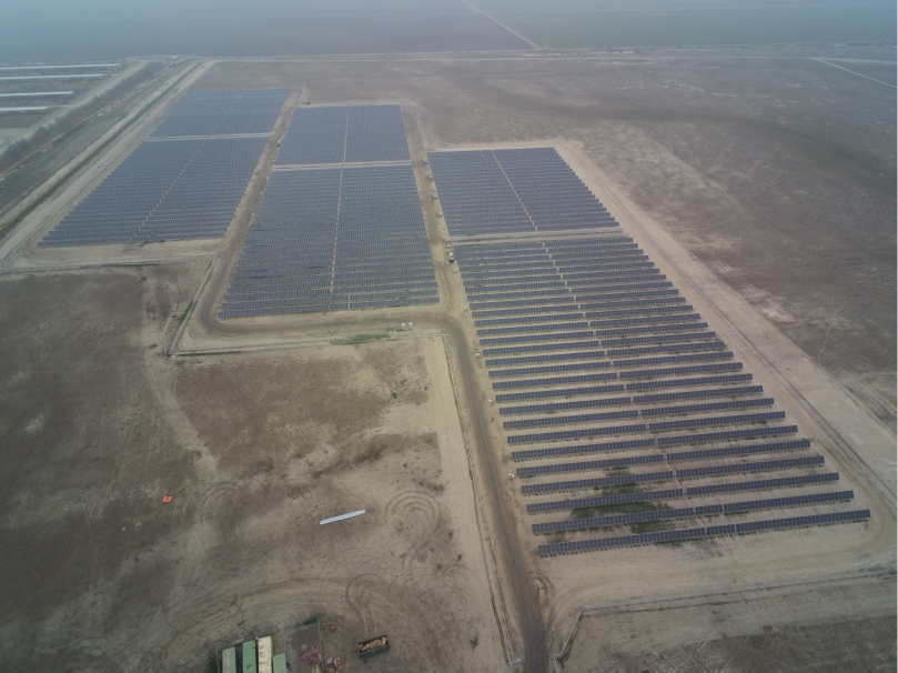 Birdseye view of three solar farms surrounded by sparse land and shrubs.