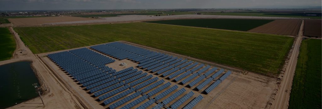 Birdseye view of field of rows of blue solar panels surrounded by green fields.