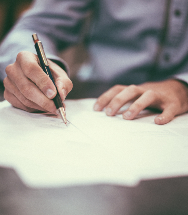 Up close image of a man's hands signing a document with a pen.