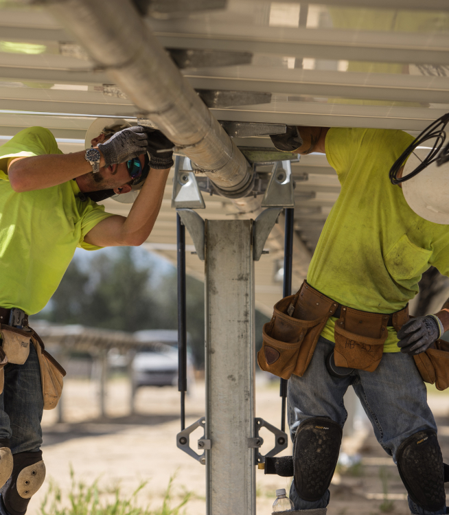 Two technicians wearing hard hats and vests assembling solar panels.