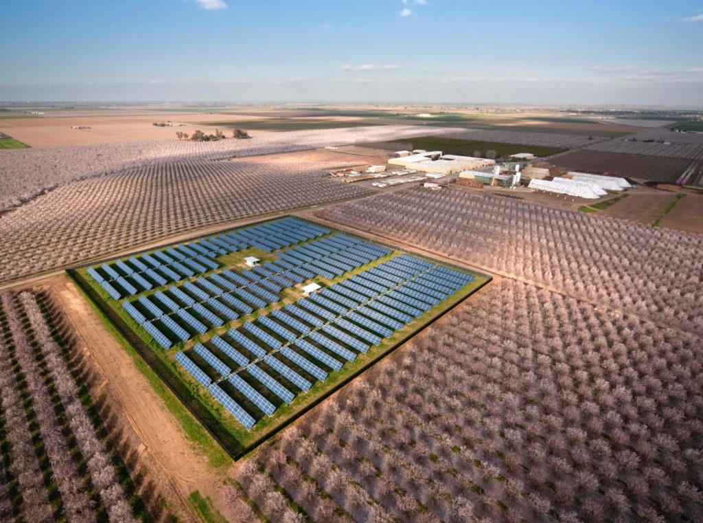 Birdseye of solar farm and building near farming fields Birdseye view of sunny solar farm and farm building with farming fields in the distance