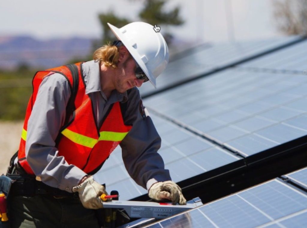 Solar technician installing a solar panel Solar technician in an orange vest and hardhat installing a solar panel