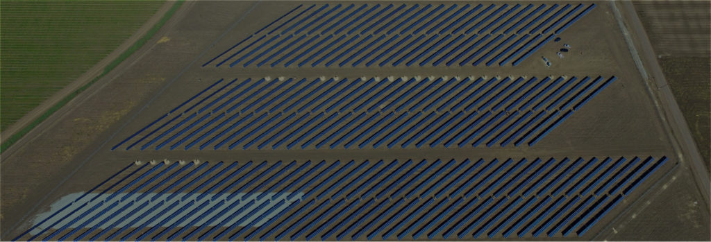 Aerial view of three rows of solar panels on farmland.