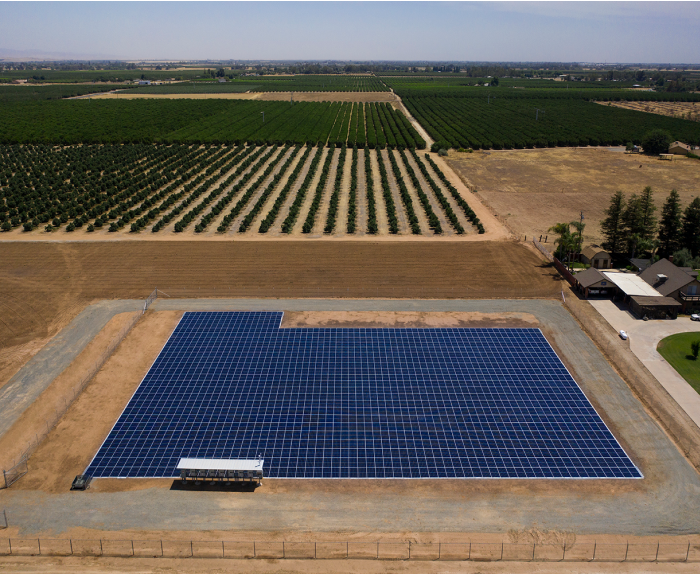 Birdseye view of large solar farm with rows of solar panels with a farm in the background