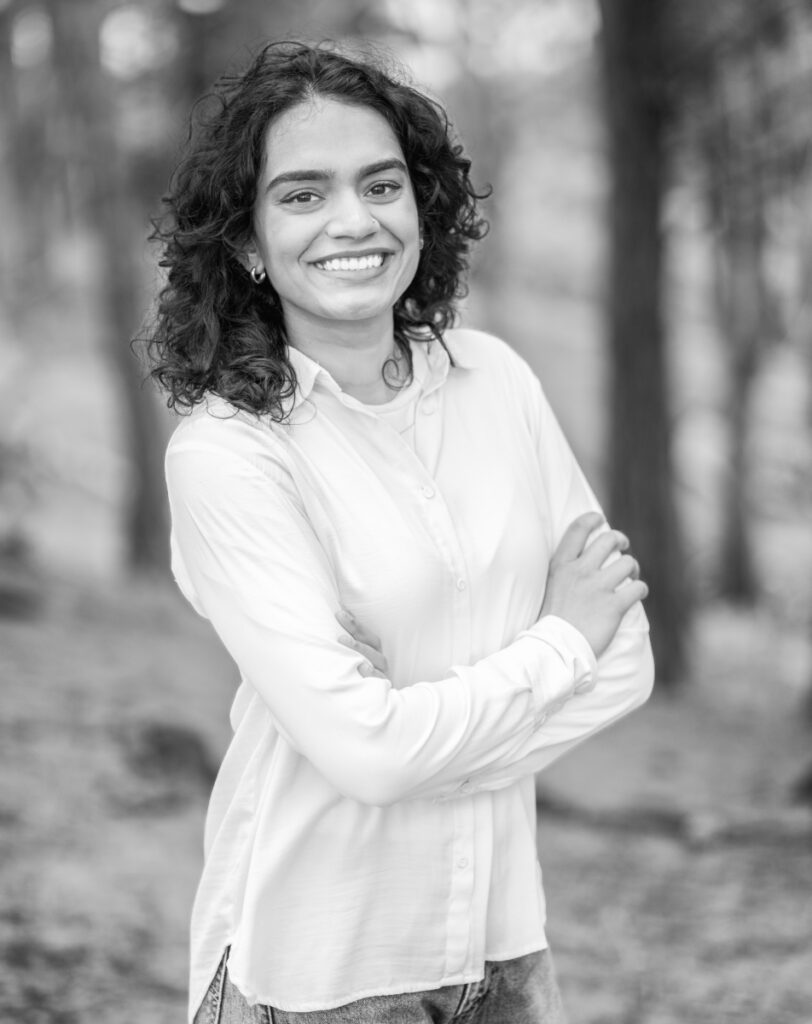 Black and white portrait of a woman with curly hair smiling outdoors.
