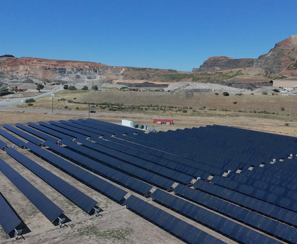 vulcan-lake-herman-350x287 Ground-mounted solar panel installation situated near an active quarry and mountain backdrop.